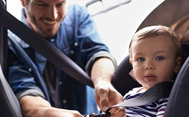 En pappa sätter fast sitt barn i bilbarnstol