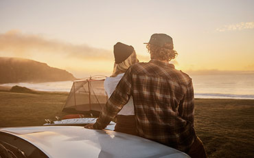 Par sitter på motorhuven och tittar ut mot havet i solnedgången